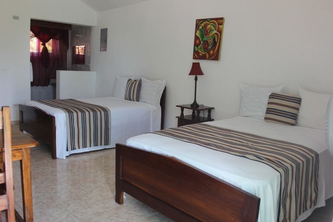 A hotel room with two beds, a wooden chair, a small table, a lamp, and a painting on the wall.
