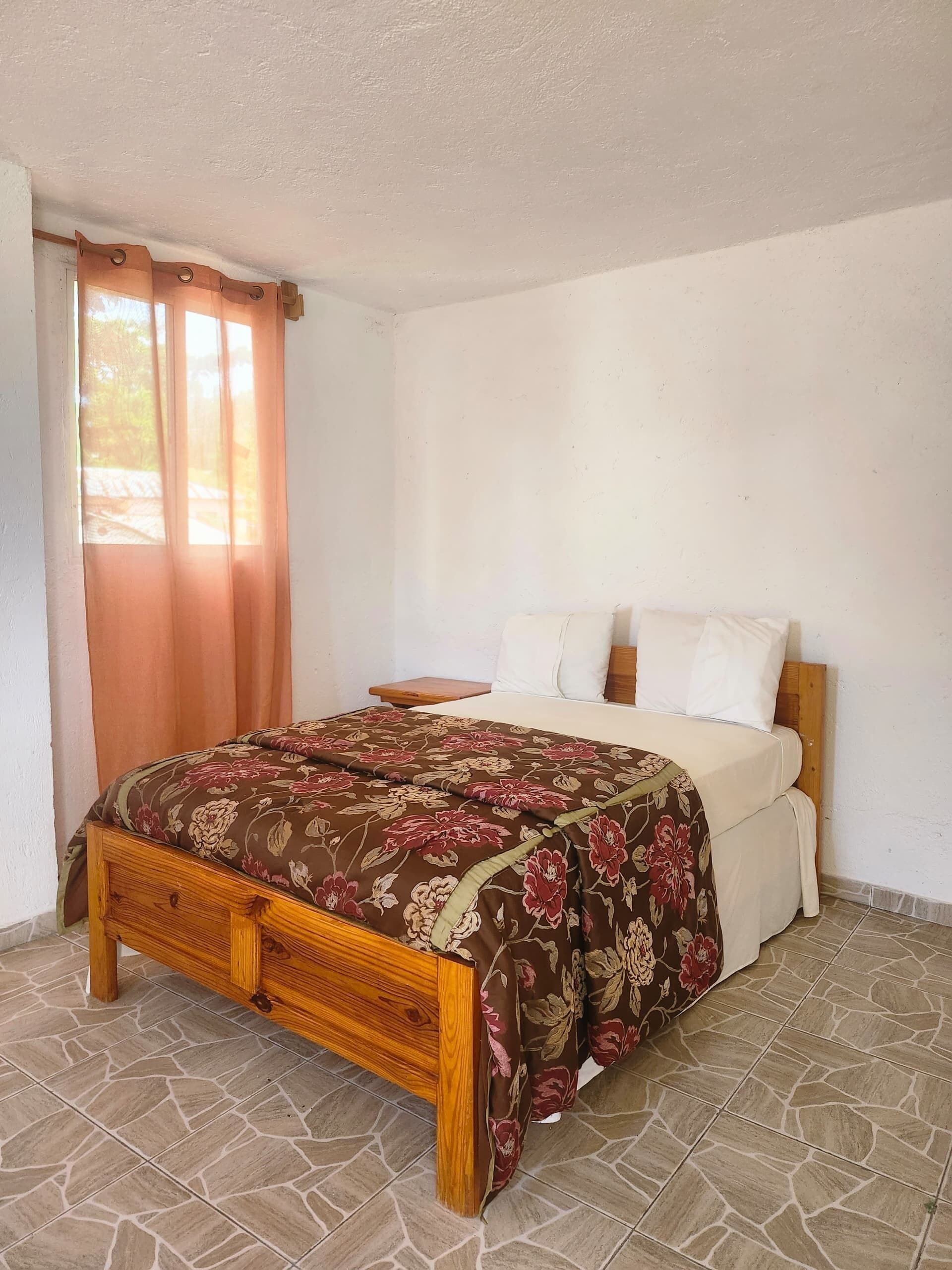 A bedroom with a wooden bed frame, a floral bedspread, and a nightstand.