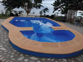 Una piscina con interior azul y borde color beige, rodeada de sillas de descanso y palmeras.