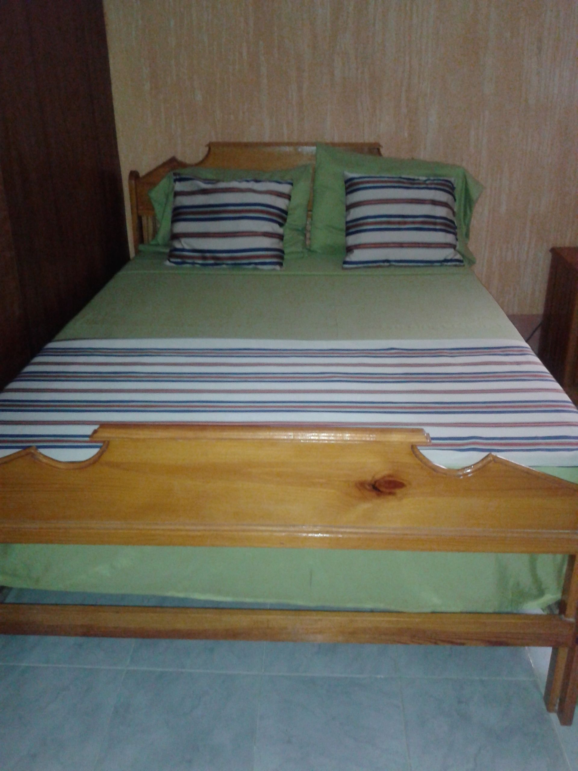 A bed with a wooden frame, green bedding, and striped pillows.