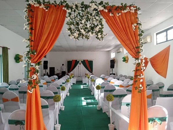 A banquet hall with rows of white chairs, green carpeting, and orange drapes.