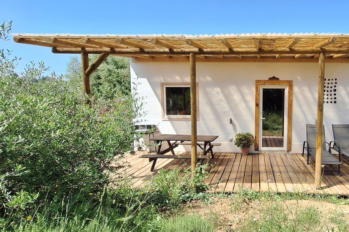 Un petit bâtiment d’un seul étage, doté d’une terrasse en bois, d’un patio couvert et d’une porte donnant sur l’intérieur.