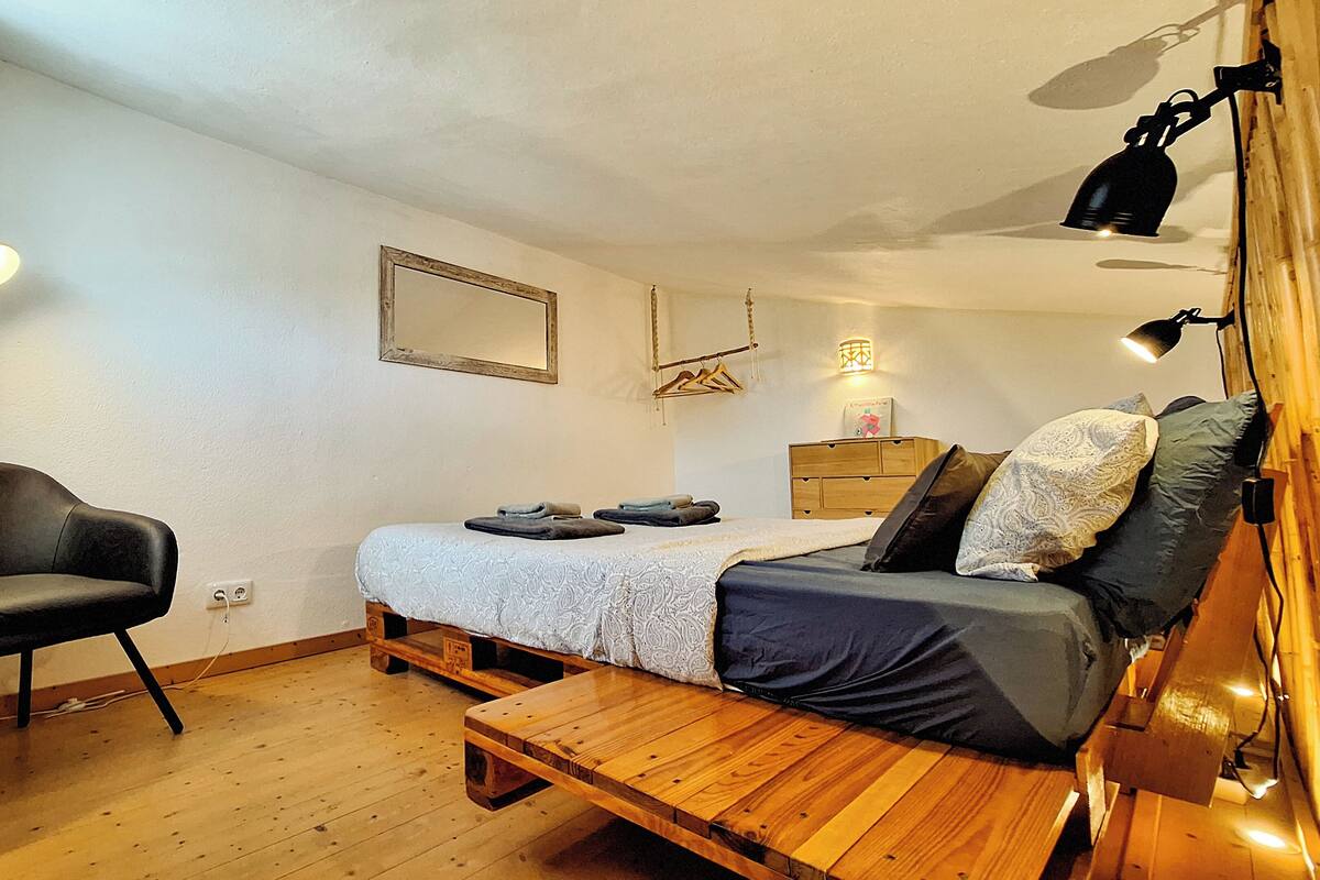 Une chambre à coucher de taille modeste, comprenant un lit, un banc en bois, une chaise et une commode.