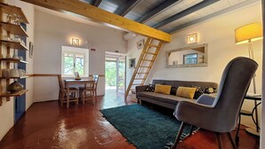 A cozy living room with a sofa, a chair, a table with chairs, shelves with glassware, a ladder, and a large mirror on the wall. - Quinta da Fornalha (Castro Marim)