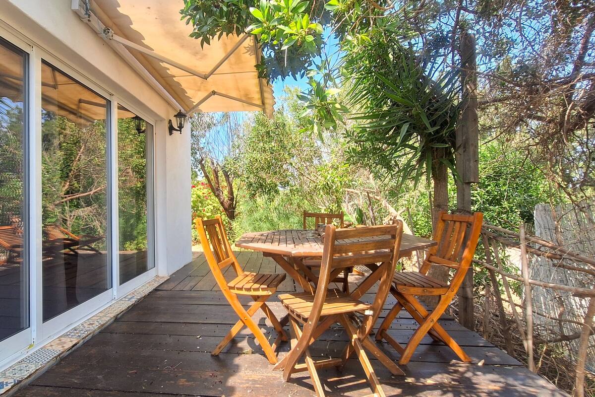 Une terrasse en bois avec une table et des chaises, un patio couvert et une vue sur la verdure et les arbres.