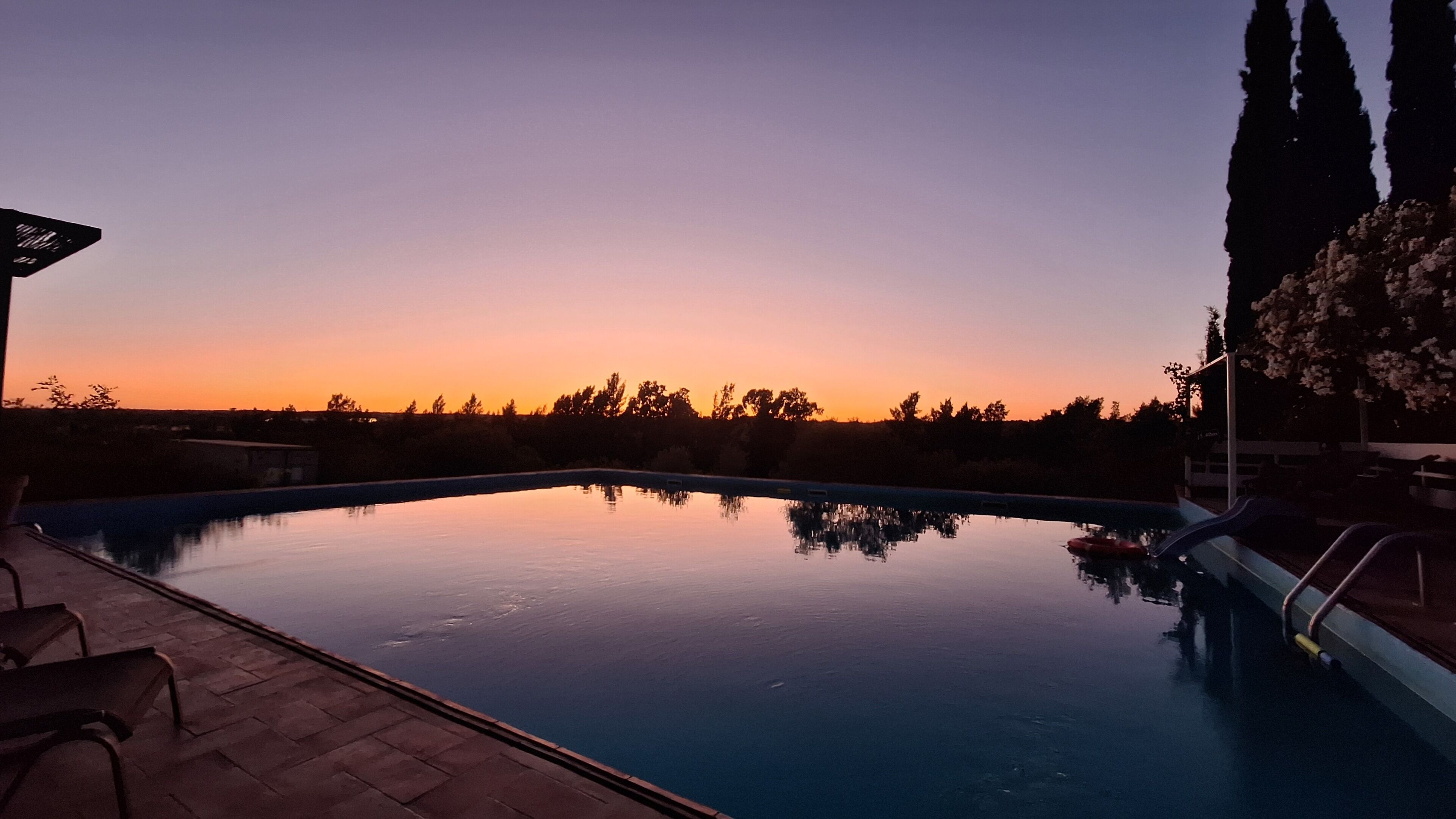 Una piscina con vista al atardecer, rodeada de árboles y un área de patio.