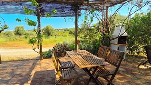 An outdoor patio with a wooden table and chairs, a grill, and a pergola with vines. - Quinta da Fornalha (Castro Marim)
