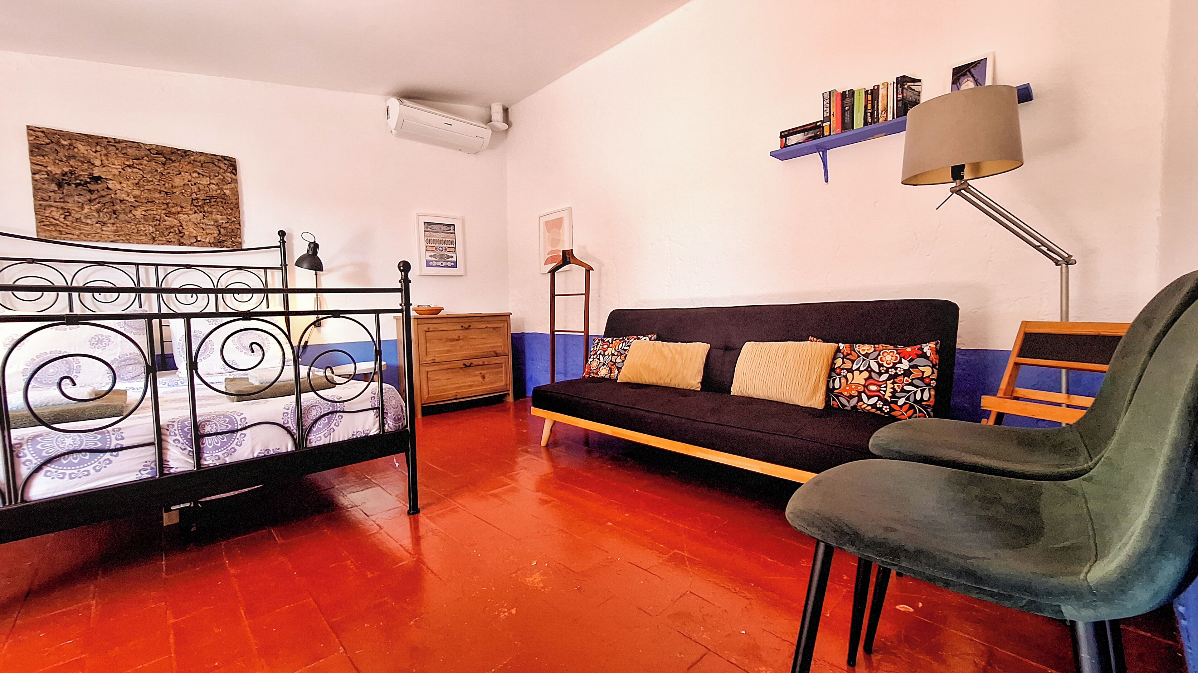 A room with a bed, a sofa, a chair, a bookshelf, and a desk.