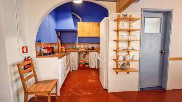 A compact kitchen with a blue archway, wooden shelves, and a door with a window.