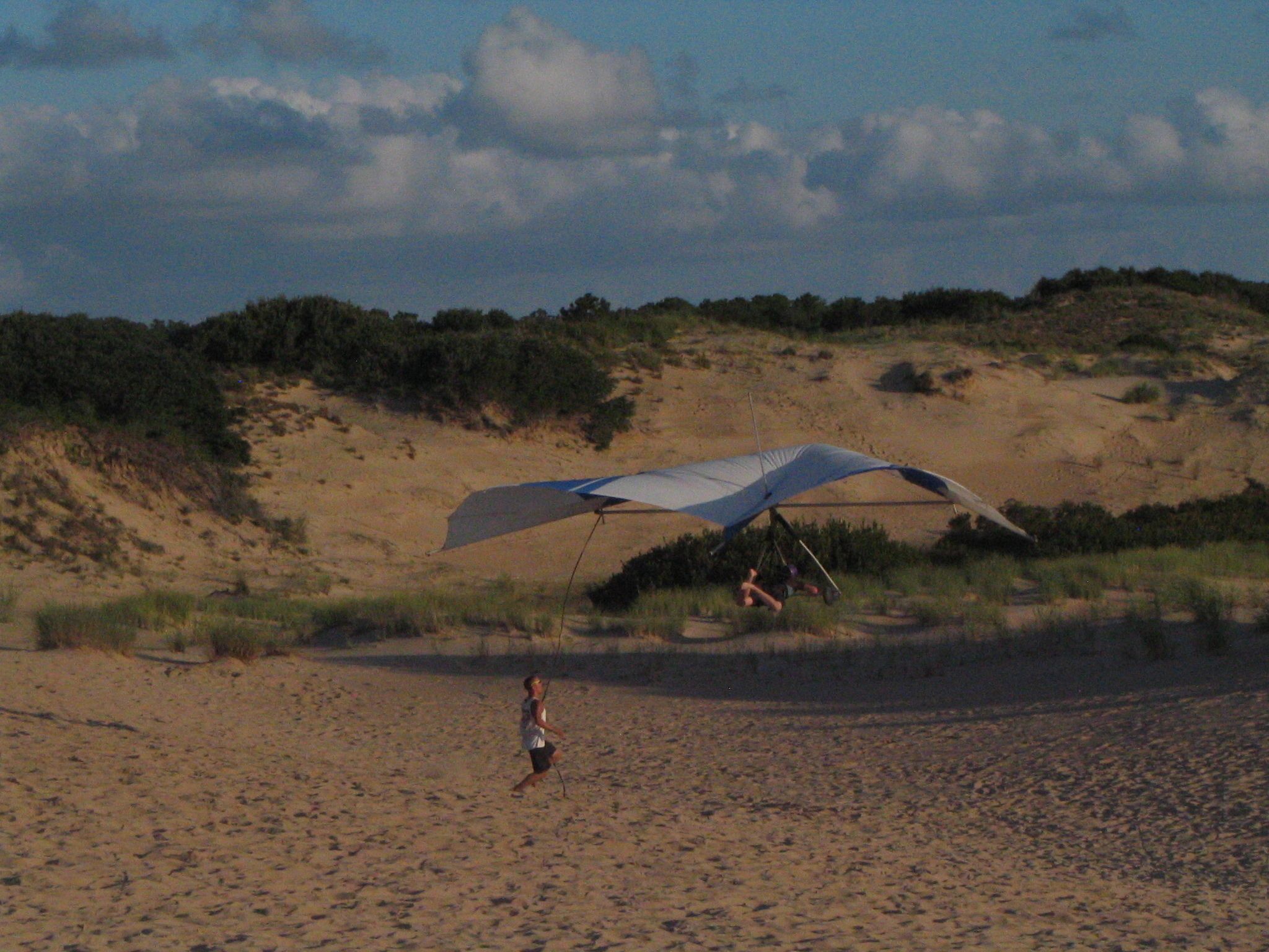 A person walking on a sandy beach with a large umbrella providing shade.