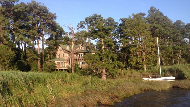A house by a river with a boat docked nearby. - Cypress Moon Inn (Kitty Hawk)