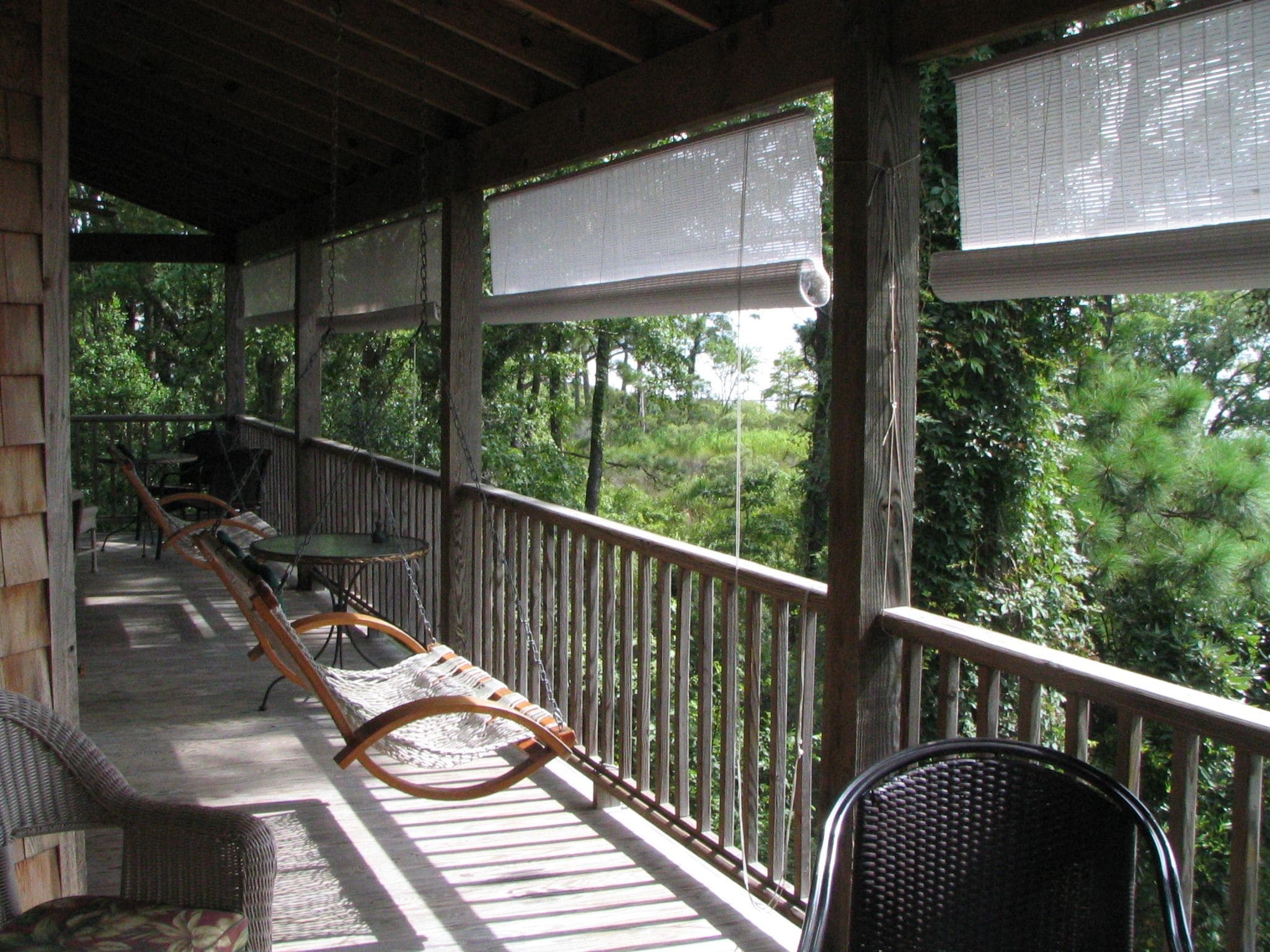 Une véranda en bois avec une chaise suspendue, une table à manger et des chaises.