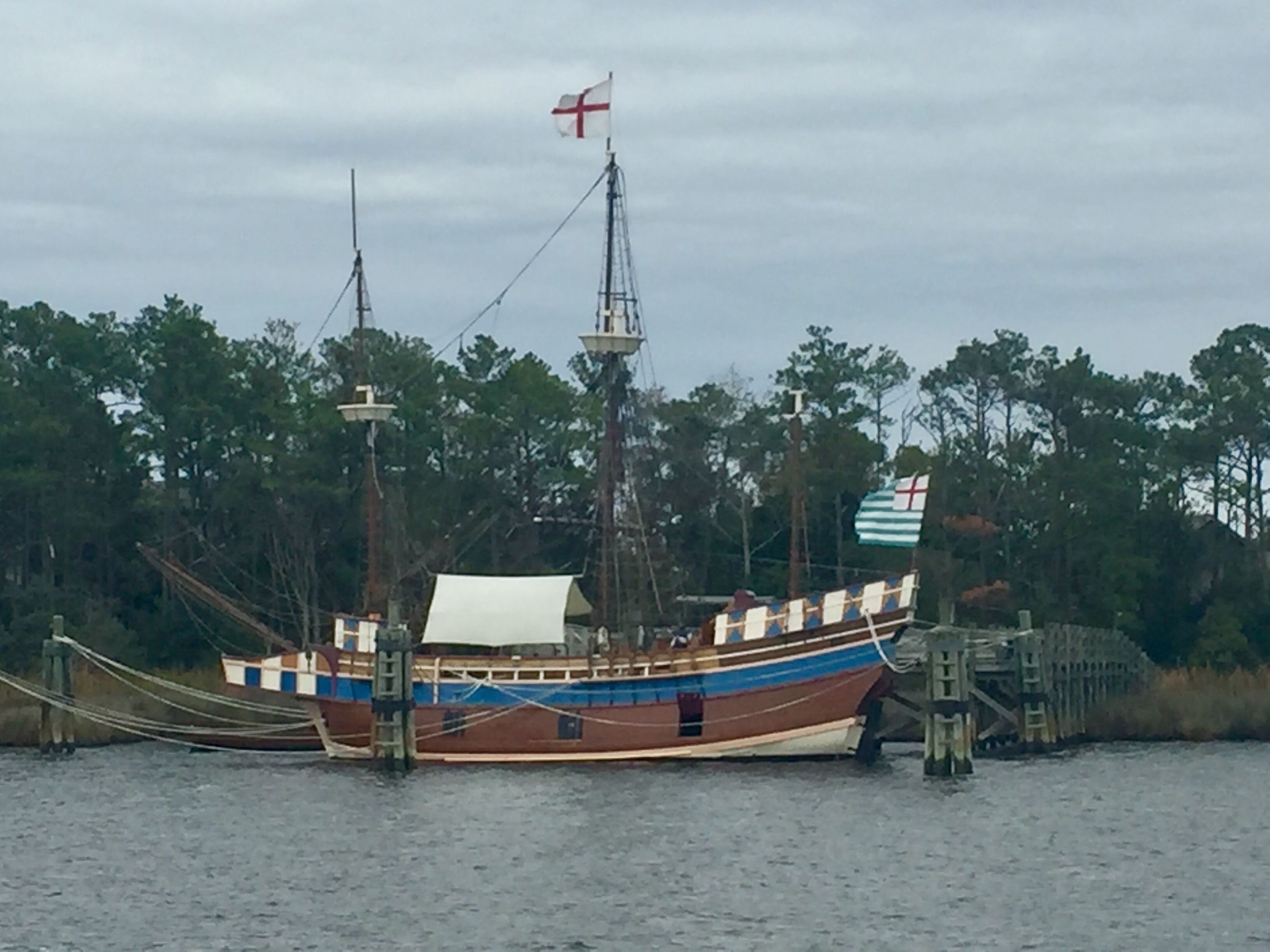 A traditional wooden boat docked at a pier with a flag and a flagpole.