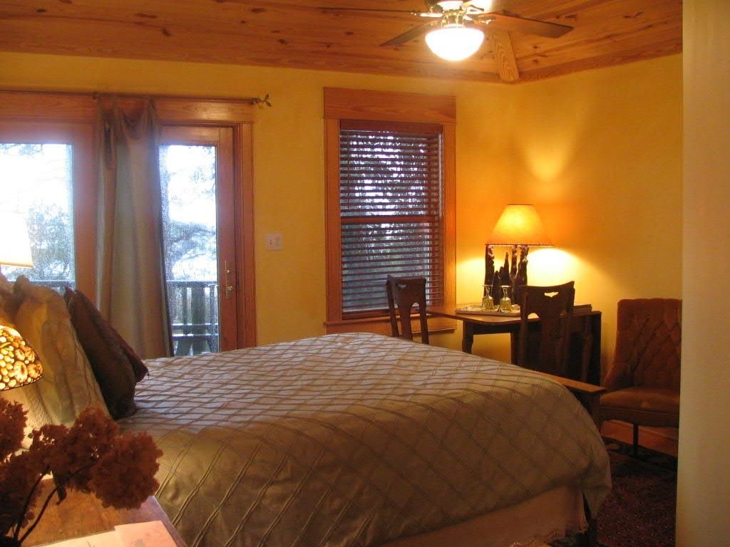 A bedroom with a bed, a desk, a chair, a lamp, and a window with blinds.