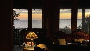 A cozy room with a view of the sea, featuring a lamp, a plush armchair, and a small table. - Cypress Moon Inn (Kitty Hawk)