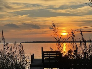 A wooden pier extending into a calm body of water, with a sunset in the background.