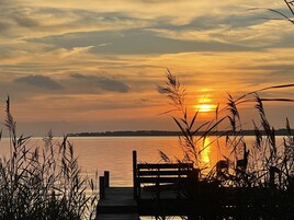 Un muelle de madera que se adentra en un cuerpo de agua tranquilo, con un atardecer al fondo.