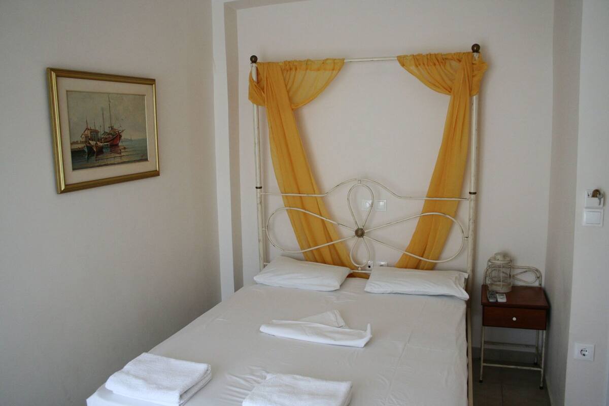 A neatly made bed with white linens and pillows, a metal headboard, and a painting on the wall.