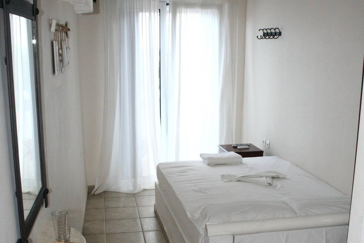A bedroom with a bed, a chair, a bedside table, a mirror, and curtains.