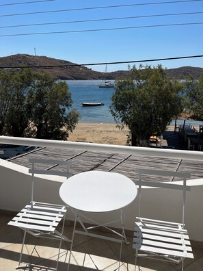 A terrace with a table and chairs, overlooking a beach with boats and trees.