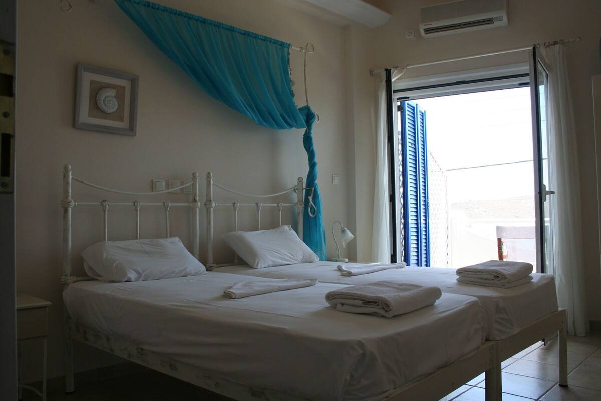 A bed with white linens, a blue curtain, and a framed picture on the wall.