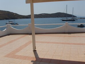 A terrace with tiled flooring, a white railing, and a view of boats on the water.