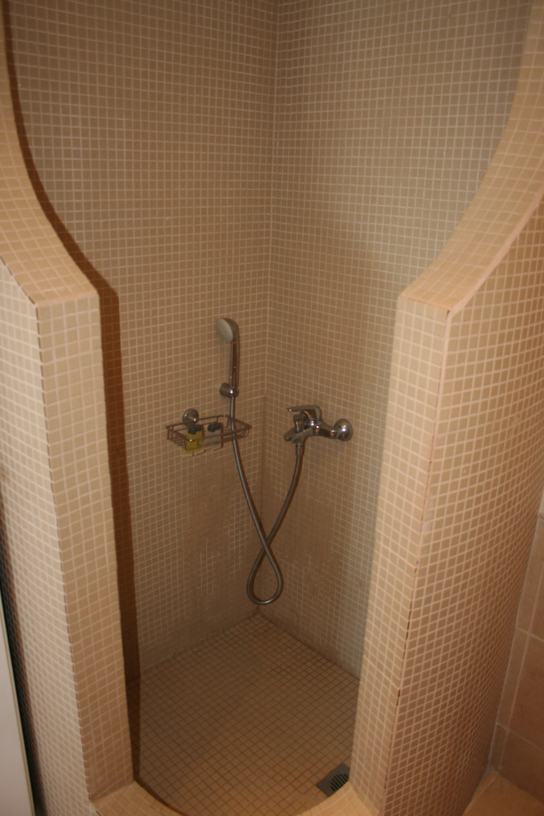 A small, tiled shower stall with a handheld showerhead and a wall-mounted faucet.