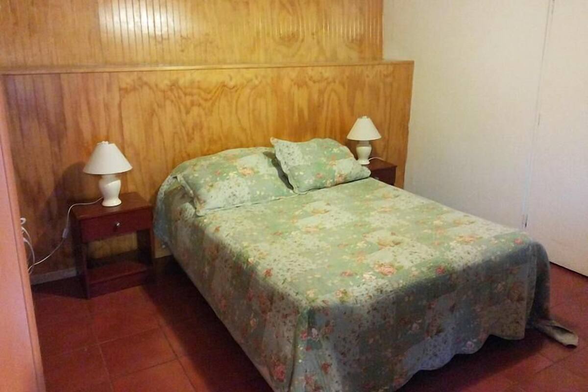A single bed with a floral bedspread, two bedside tables with lamps, and wooden paneling on the walls.