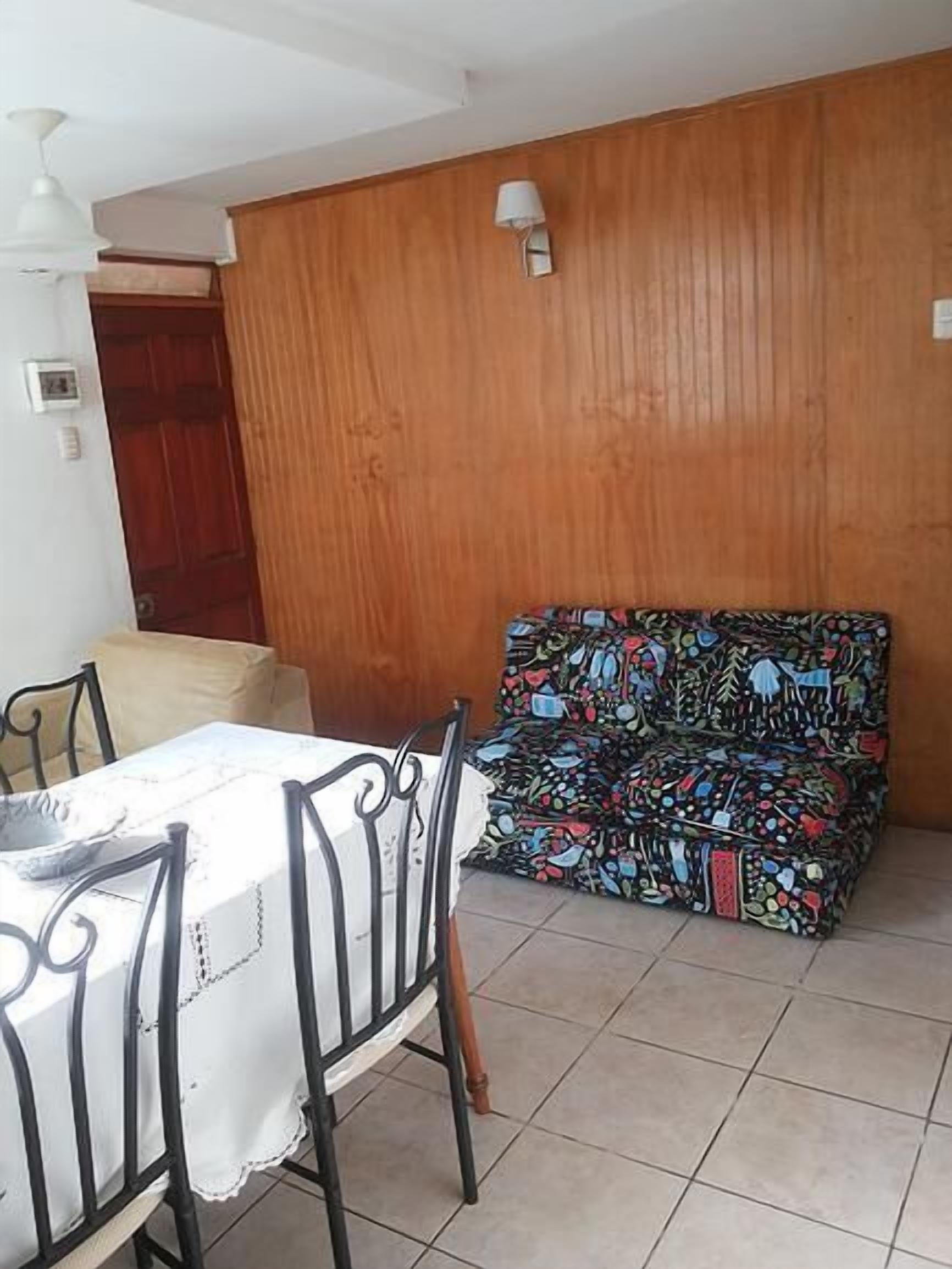 Un comedor con una mesa y sillas, un sofá estampado, paneles de madera y un ventilador de techo.