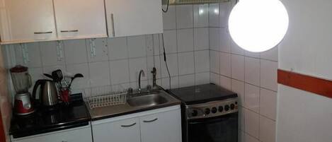 A compact kitchen with white cabinets, a stove, a sink, and a blender.