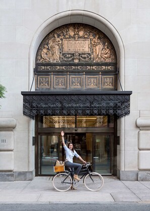 Una persona en bicicleta frente a un edificio con una amplia entrada arqueada y ornamentación metálica.