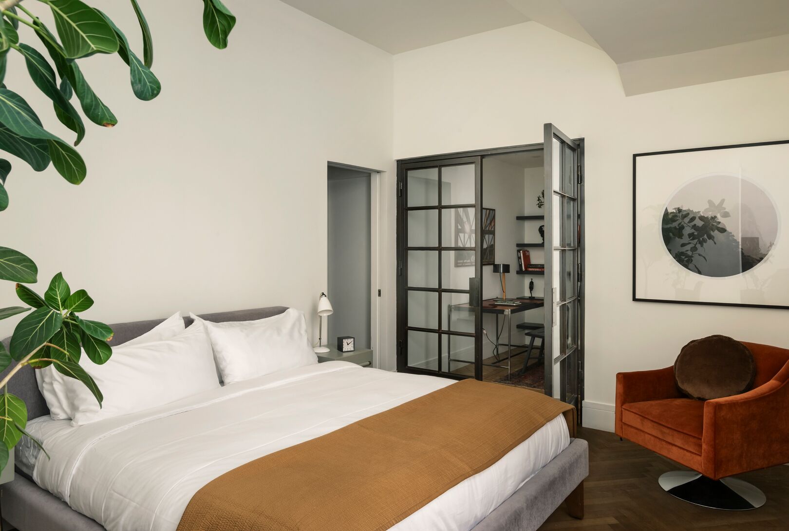 A hotel room with a bed, a chair, a desk, and a bookshelf.