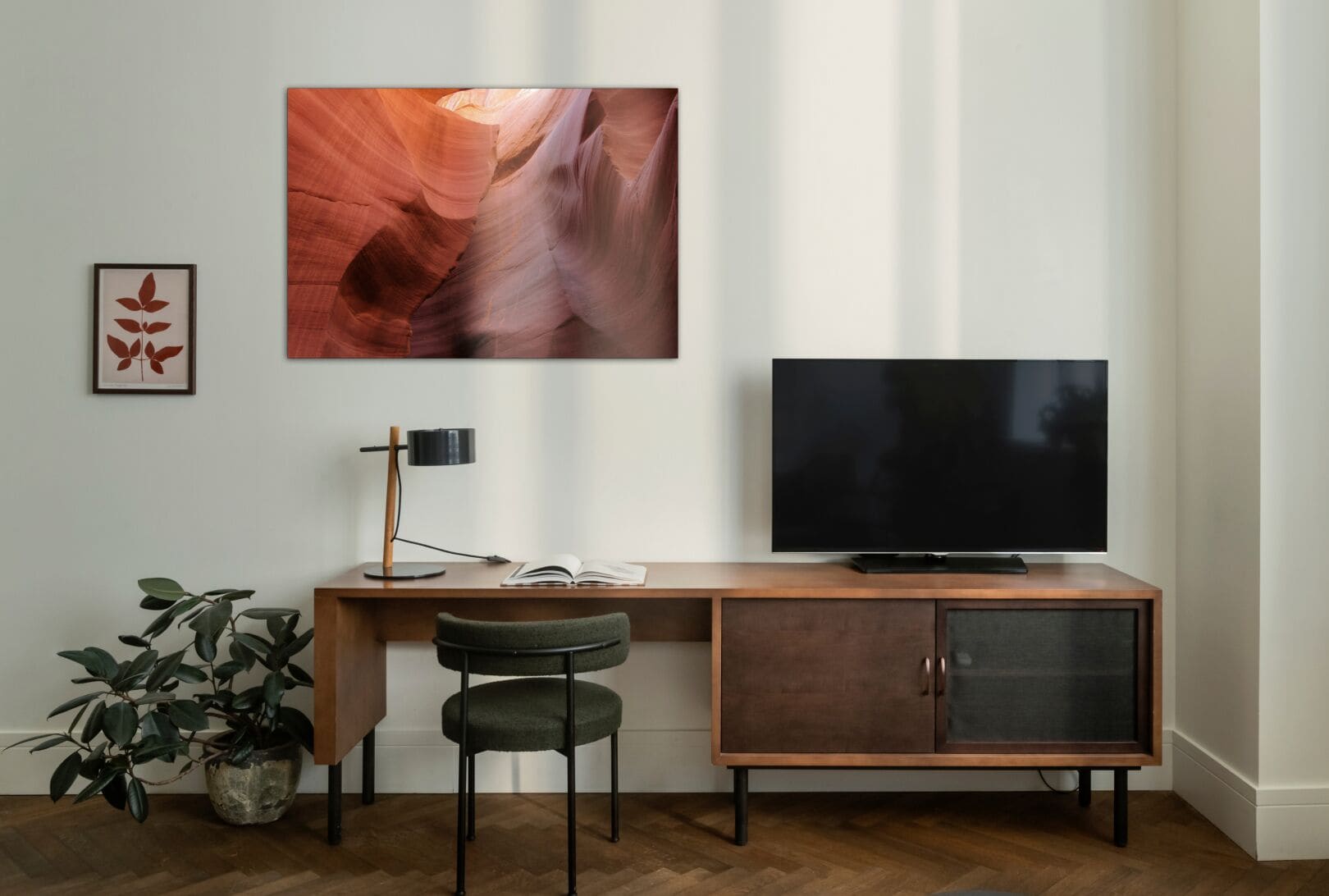 A modern living room with a wooden desk, a television, a plant, and a framed picture on the wall.