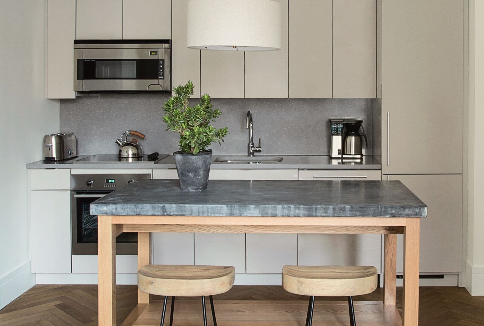 A modern kitchen with a built-in microwave, a kettle, a coffee maker, and a potted plant on the island.