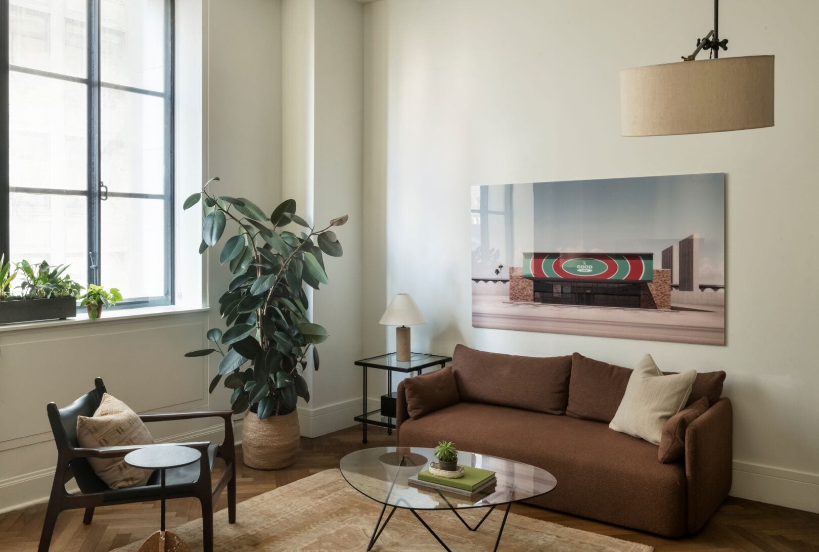 A living room with a brown sofa, a glass coffee table, a potted plant, and a painting of a building.