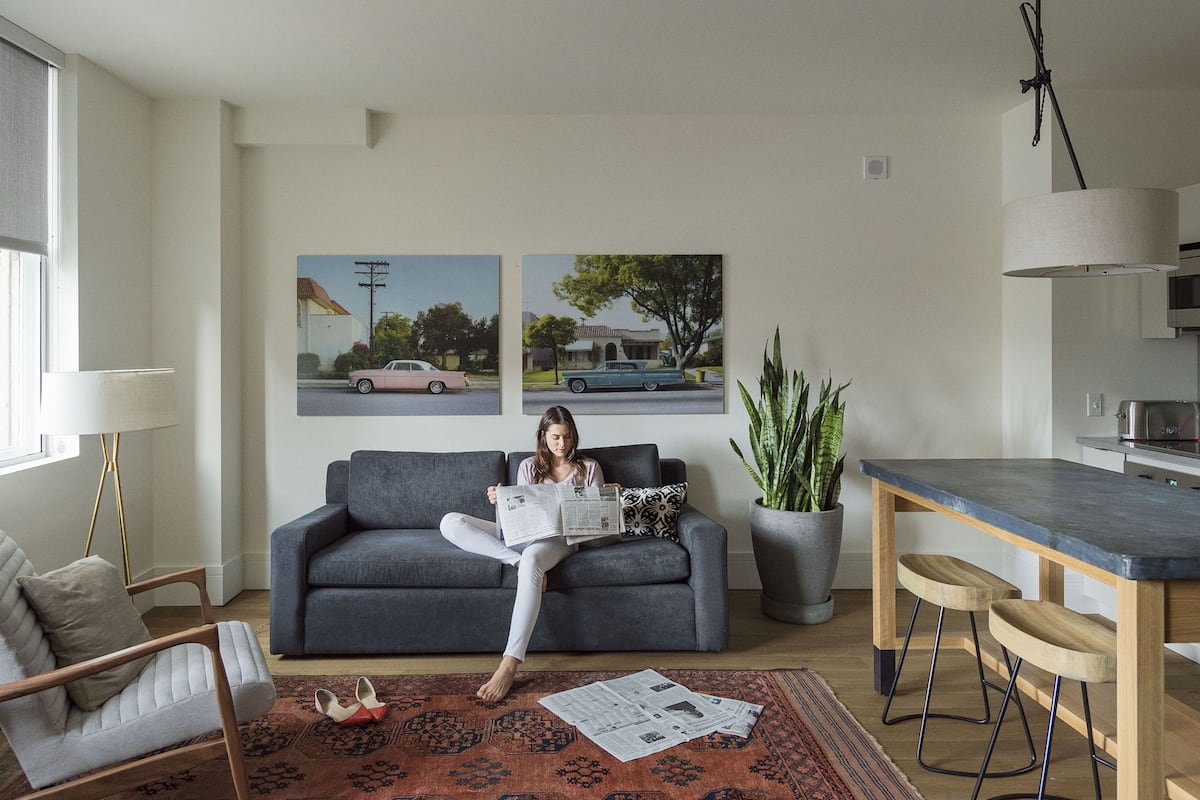 A modern living room with a grey sofa, a coffee table, a dining area with bar stools, and a kitchen in the background.