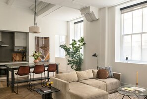 En moderne stue med sofa, spisebord, stole og et stort vindue.