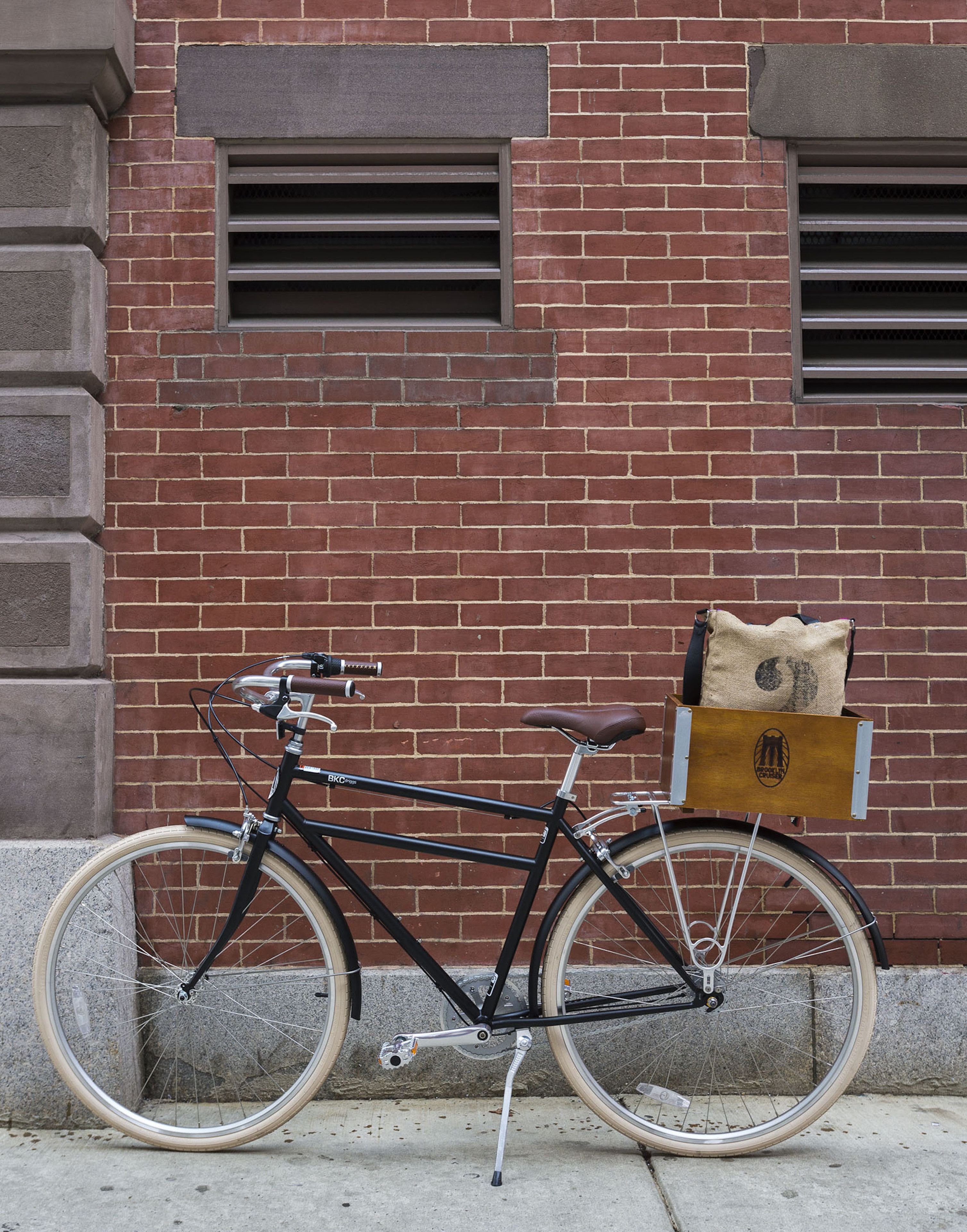 A bicycle parked against a brick wall with a box containing a pillow on the back.