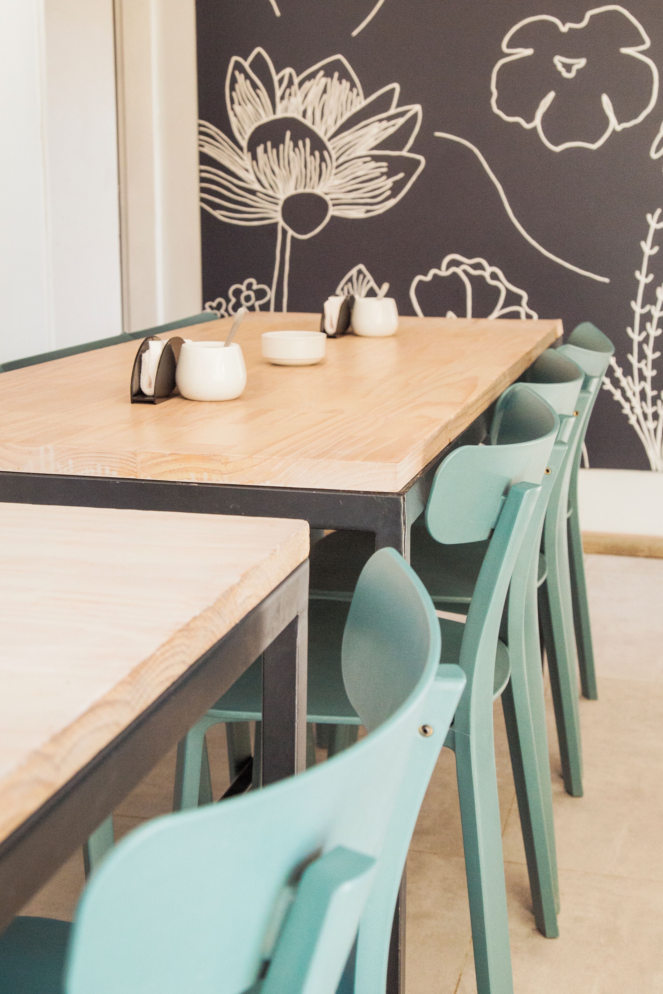 A wooden dining table with teal chairs, a white teapot, and a cup on it.