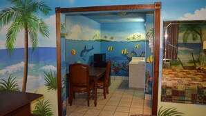 A room with a beach-themed mural, a wooden dining table, and a bed with a patterned bedspread. - Economy Inn (New Orleans)