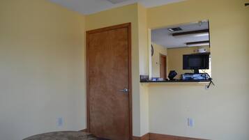 A room with a wooden door, a small round table, a built-in shelf with a computer setup, and a wall-mounted mirror.