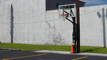 Ein Basketballkorb ist an einer Betonwand angebracht, und eine Treppe führt zu einer Tür.