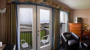Una habitación con vistas al mar a través de un ventanal, un aparador de madera, un sillón de cuero y una mesita.