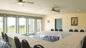 Un salón de conferencias con una gran mesa, sillas y un televisor sobre un escritorio. Hay ventanas con vistas al exterior.