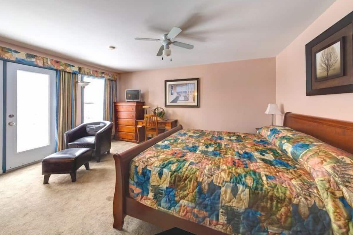 A bedroom with a bed, a chair, a dresser, a ceiling fan, and a door.