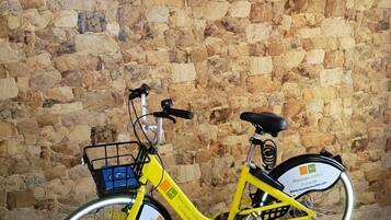 Ein gelbes Fahrrad mit Korb und einem Schild hinten, abgestellt vor einer Steinmauer. Auf der Mauer sind die Worte "MUSTIQUE SUITES" zu sehen.