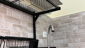 A kitchen with a stainless steel sink, a black wire rack, and a brick wall.