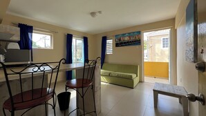 A room with a dining area featuring a table and chairs, a green sofa, and a painting on the wall.