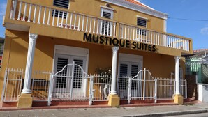 A yellow building with a balcony and a sign that reads "MUSTIQUE SUITES".