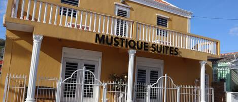 A yellow building with a balcony and a sign that reads "MUSTIQUE SUITES".
